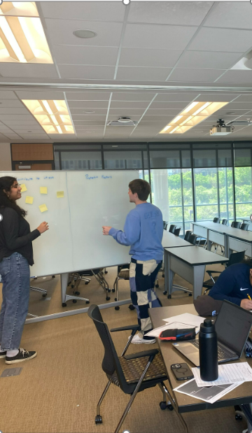 2 teens standing, young woman and young man, looking at a whiteboard