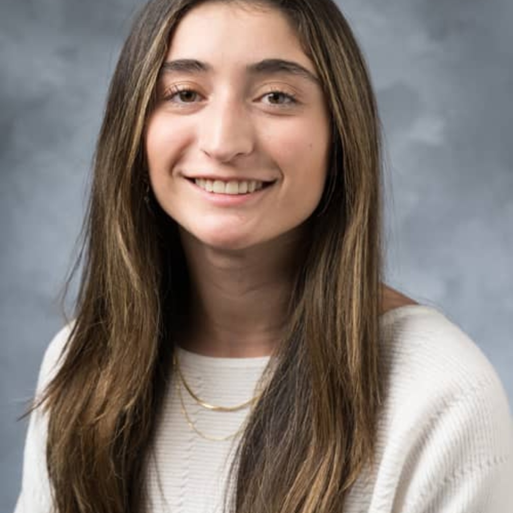 Picture of Isabella, blue background, long brown hair, cream sweater, smiling at the camera.