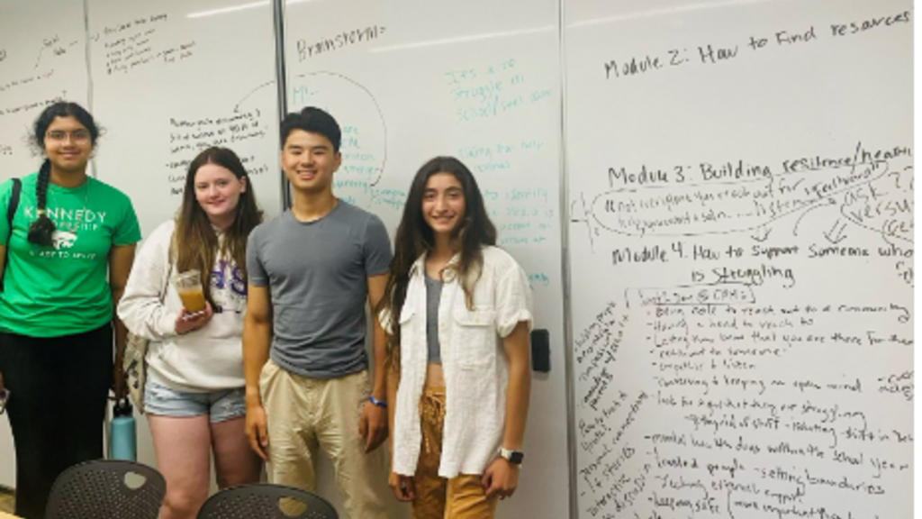 4 teens standing in front of a white board, dressed casually 
